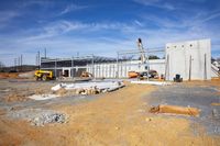 an unfinished building being constructed on a sunny day on a farm near a highway construction site