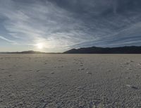 a lone skiboarder is seen walking through the desert under the setting sun with tracks left on the snow