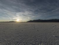 a lone skiboarder is seen walking through the desert under the setting sun with tracks left on the snow