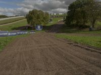 a dirt course with signage and two dirt roads leading up to it on a hill