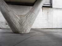 an upside down concrete structure sits on the cement floor with a white wall behind it