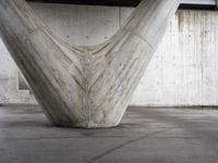 an upside down concrete structure sits on the cement floor with a white wall behind it