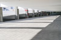 a long hallway with a railing and a line of parked cars in it, inside an airport