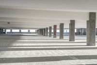 a long hallway with a railing and a line of parked cars in it, inside an airport