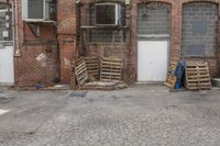 several crates and one blue bag in front of a building with windows and some closed doors