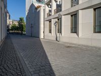 two people walking down an empty city street in an alley area with tall buildings in the background