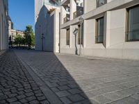 two people walking down an empty city street in an alley area with tall buildings in the background