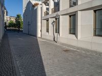 two people walking down an empty city street in an alley area with tall buildings in the background