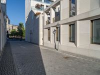 two people walking down an empty city street in an alley area with tall buildings in the background