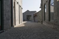 the person is walking down the street near old buildings on a sunny day with a red umbrella