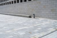 a stone wall sits in the middle of a brick walkway and sidewalk in front of a building with glass windows