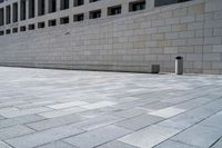 a stone wall sits in the middle of a brick walkway and sidewalk in front of a building with glass windows