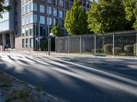 a man riding his skateboard down a long road next to a building with a metal fence