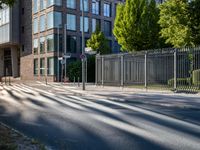 a man riding his skateboard down a long road next to a building with a metal fence