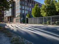 a man riding his skateboard down a long road next to a building with a metal fence