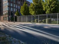 a man riding his skateboard down a long road next to a building with a metal fence