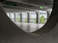 a view through a hole in an indoor parking space, towards a street and building