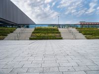 an outdoor area with hedges and stairs, and other buildings in the distance below a cloudy sky