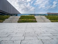 an outdoor area with hedges and stairs, and other buildings in the distance below a cloudy sky