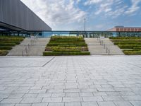 an outdoor area with hedges and stairs, and other buildings in the distance below a cloudy sky