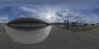 a fish eye view of an outdoor city, showing the sky and clouds with building on top and a street with trees