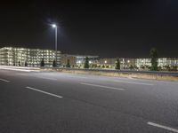 an empty highway at night with lights above the building and surrounding it and a building near by