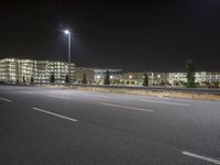 an empty highway at night with lights above the building and surrounding it and a building near by