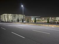 an empty highway at night with lights above the building and surrounding it and a building near by