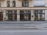 a empty street next to a stone building with glass windows, there is no one standing on either side