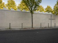 the side of a building with trees and a fence behind it, near a paved street