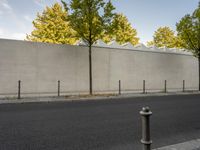 the side of a building with trees and a fence behind it, near a paved street