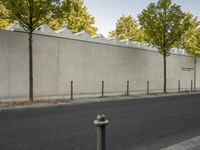 the side of a building with trees and a fence behind it, near a paved street