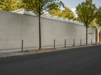 the side of a building with trees and a fence behind it, near a paved street