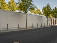 the side of a building with trees and a fence behind it, near a paved street