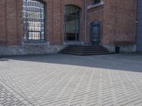 the street is paved with concrete blocks next to a brick building, with stairs and glass windows