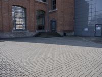 the street is paved with concrete blocks next to a brick building, with stairs and glass windows