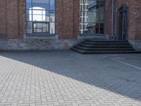 the street is paved with concrete blocks next to a brick building, with stairs and glass windows