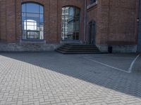 the street is paved with concrete blocks next to a brick building, with stairs and glass windows