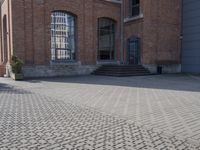 the street is paved with concrete blocks next to a brick building, with stairs and glass windows