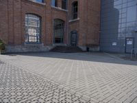 the street is paved with concrete blocks next to a brick building, with stairs and glass windows