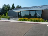 a building is surrounded by flower beds and trees and grass on the sidewalk in front of it