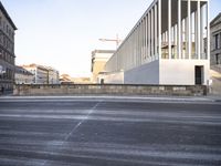 the large, empty sidewalk with multiple columns in front of the building with two signs