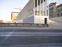 the large, empty sidewalk with multiple columns in front of the building with two signs