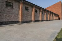 a couple of red buildings sitting next to a tall brick building with black windows and brick pillars