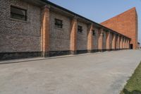 a couple of red buildings sitting next to a tall brick building with black windows and brick pillars