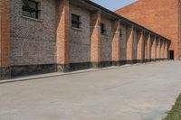 a couple of red buildings sitting next to a tall brick building with black windows and brick pillars