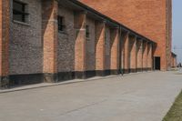 a couple of red buildings sitting next to a tall brick building with black windows and brick pillars