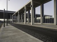 a building with metal columns and many cars parked at the roadside side and an open walkway