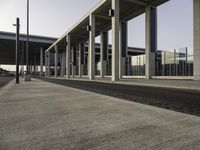 a building with metal columns and many cars parked at the roadside side and an open walkway