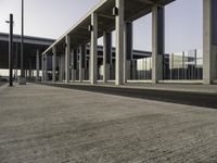 a building with metal columns and many cars parked at the roadside side and an open walkway